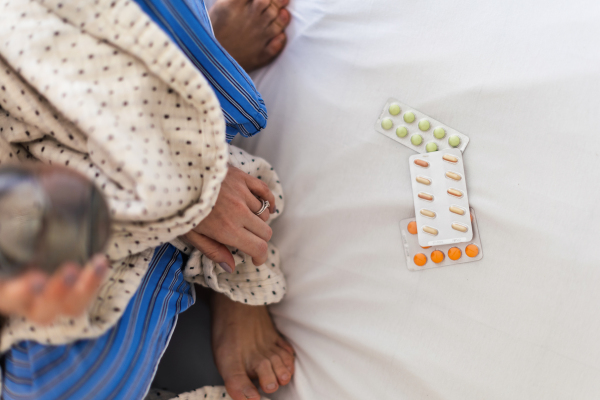 Top view of pills on a bed, nrecognizale person taking them,