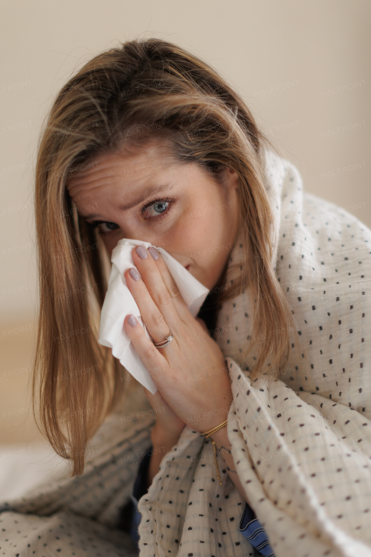 Portrait of young sick woman sneezing at her bedroom.