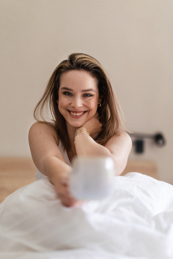 Happy woman sitting on her bed with a cup of coffee.