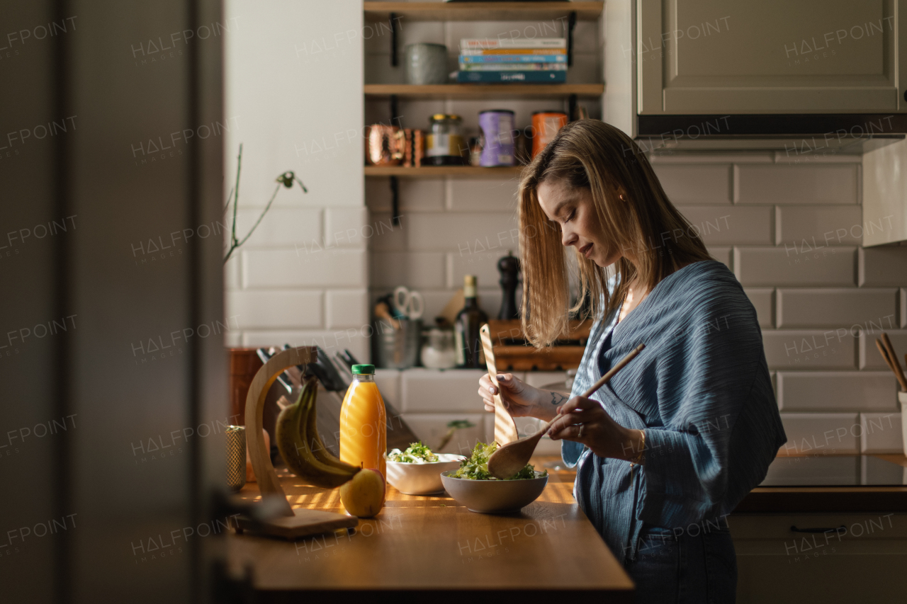 Young woman preparing salad in the kitchen.