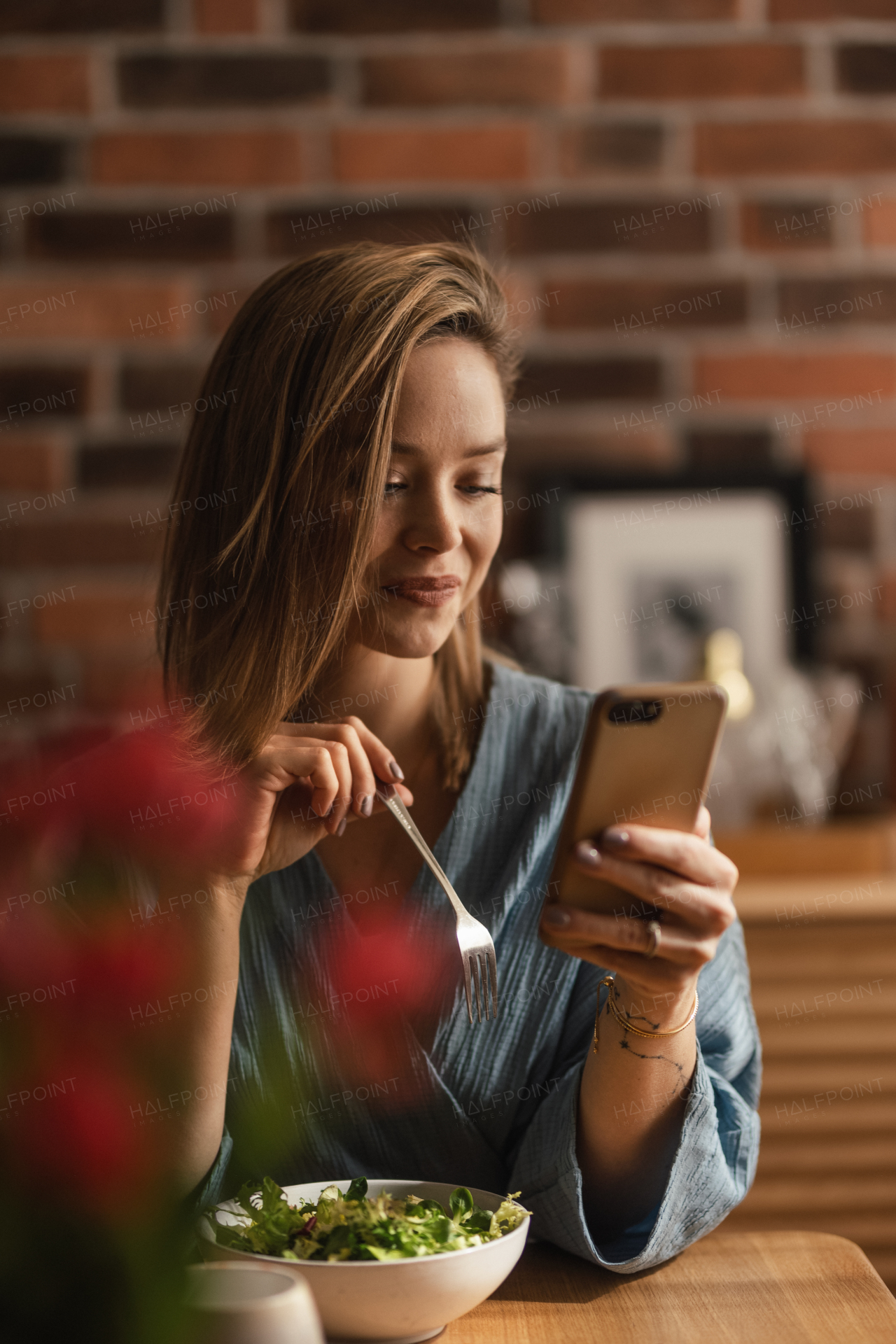 Young woman eating vegetable salad and scrolling her phone.