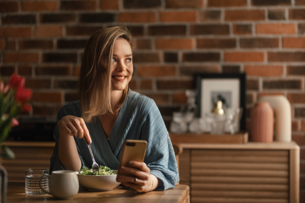 Young woman eating vegetable salad and scrolling her phone.