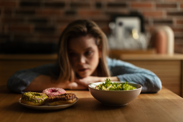 Young woman having diet, deciding between a salad and donuts.