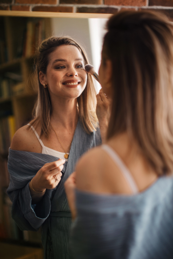 Young woman doing her make-up, looking in a mirror.