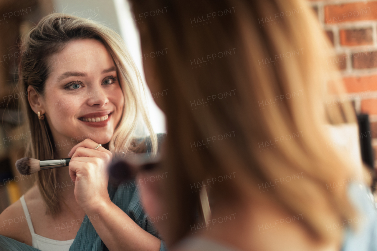 Young woman doing her make-up, looking in a mirror.