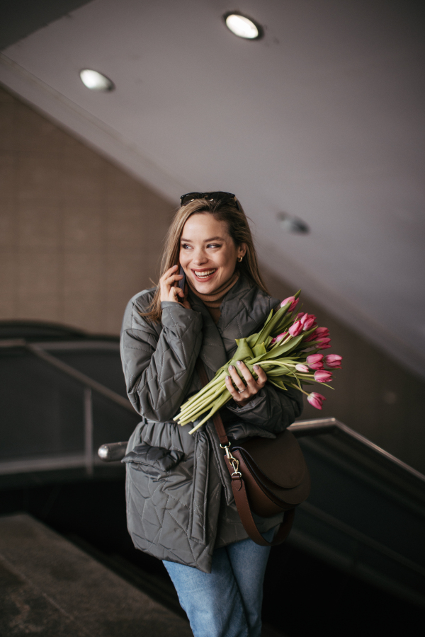 Young woman calling in a city with bouquet of tulips.