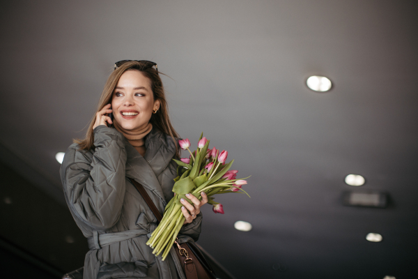 Young woman calling in a city with bouquet of tulips.