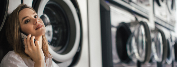 Young woman calling with smartphone, sitting in a laundry room.