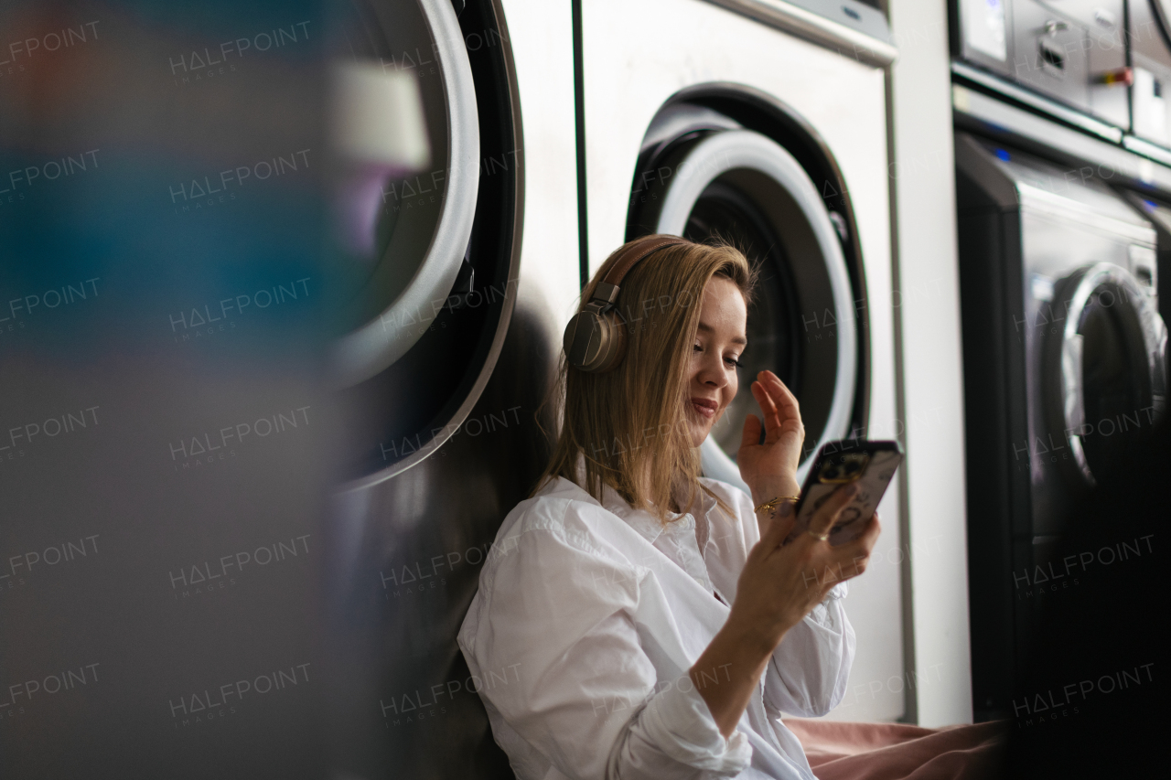 Young woman listening music, sitting in a laundry room.