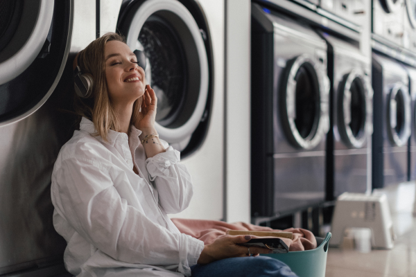 Young woman listening music, sitting in a laundry room.