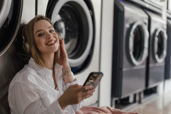 Young woman listening music, sitting in a laundry room.