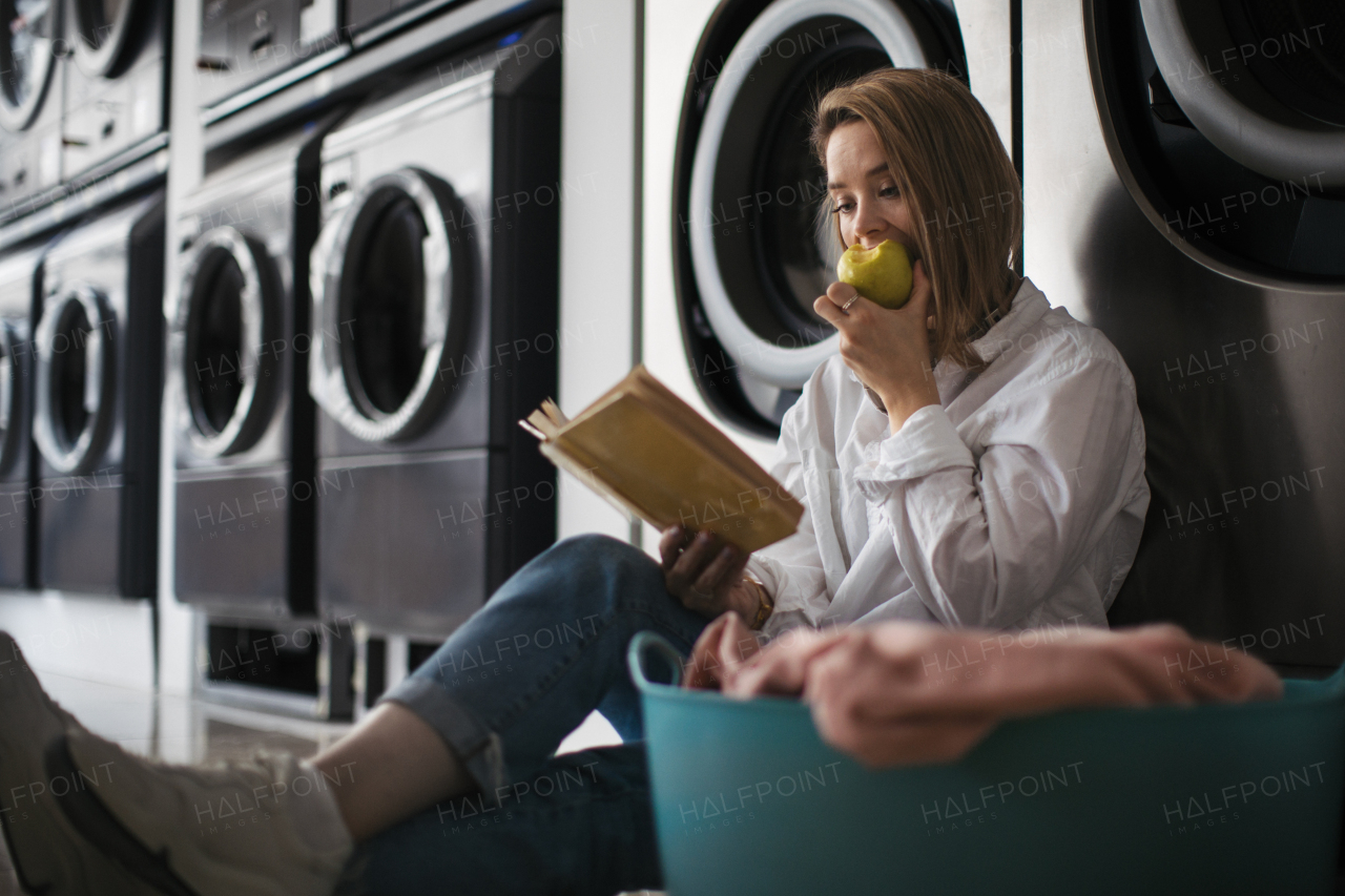 Young woman reading a book, sitting in a laundry room.