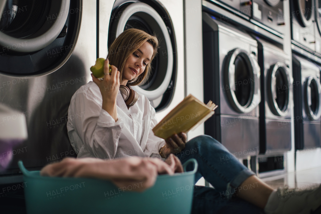 Young woman reading a book, sitting in a laundry room.