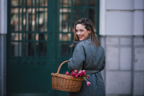 Rear view of young woman in a city with a basket full of flowers.