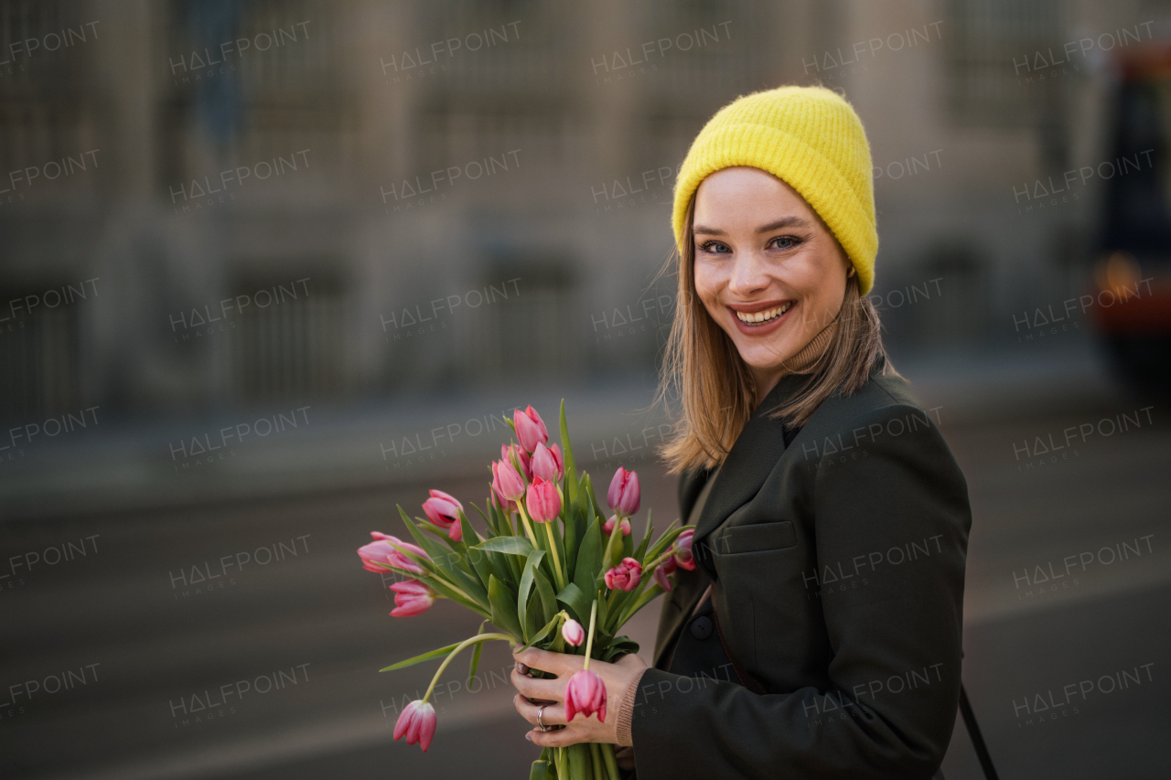 Portrait of young woman in a city with bouquet of tulips.