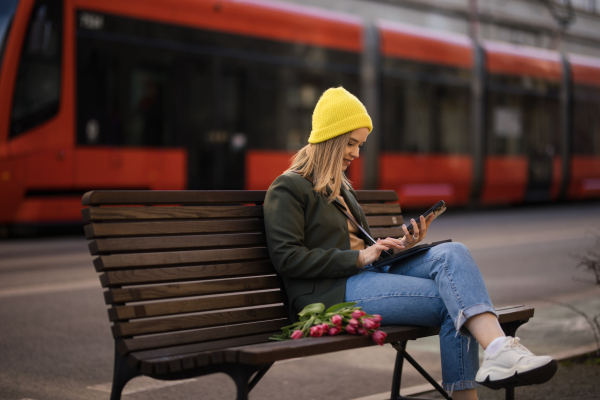 Young woman sitting in a city with tulips and digital tablet.