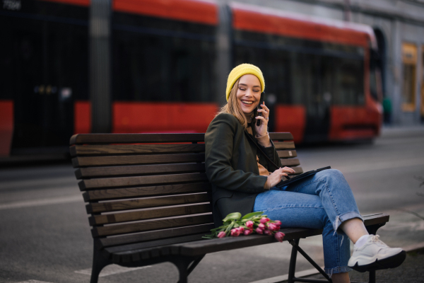 Young woman sitting in a city with tulips and digital tablet.