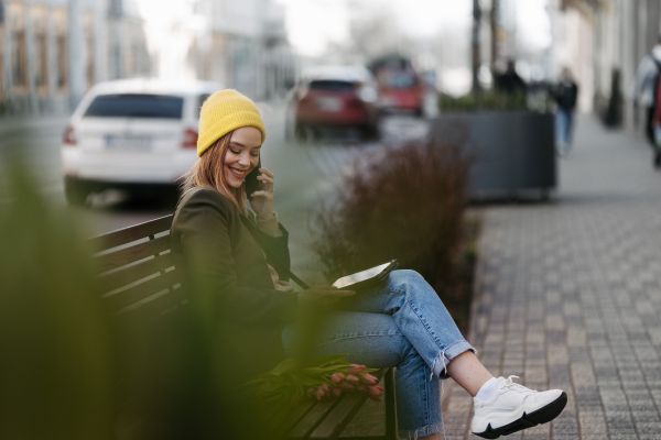 Young woman sitting in a city with tulips and digital tablet.