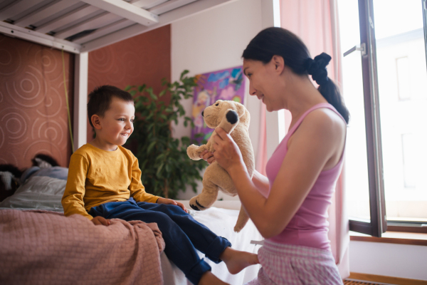 A single mother waking her son up for kindergarten in the morning. Beautiful mom awakens the preschooler with a stuffed toy, playing and making him laugh.