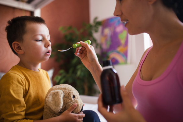 Young beautiful mother giving medicines, coughing syrup from spoon to her sick little son. Concept of children seasonal illness, viruses and kid's immune system.