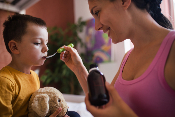 Young beautiful mother giving medicines, coughing syrup from spoon to her sick little son. Concept of children seasonal illness, viruses and kid's immune system.