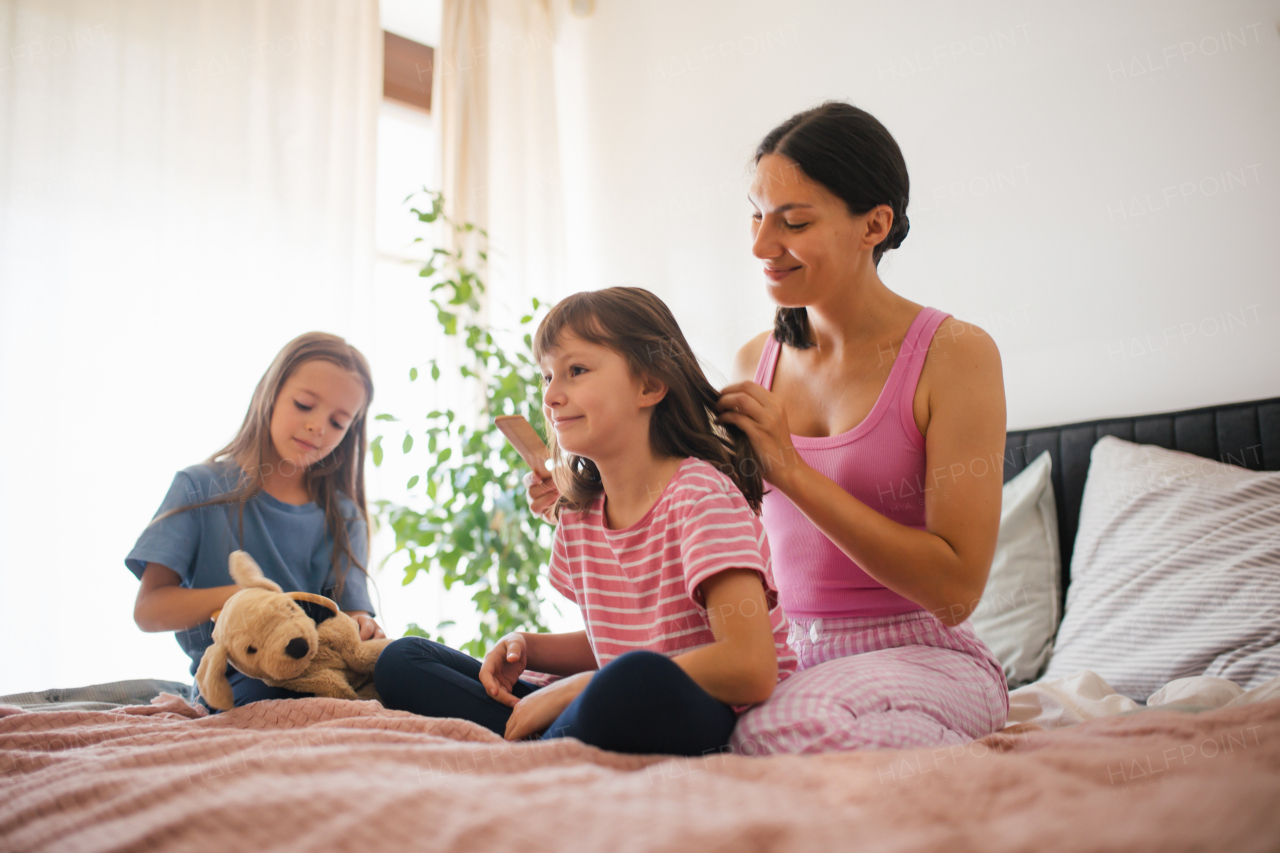 Portrait of a mother with two daughters on a bed in the bedroom. Mother combs her daughter's long hair with a comb. Concept of Mother's Day and maternal love.