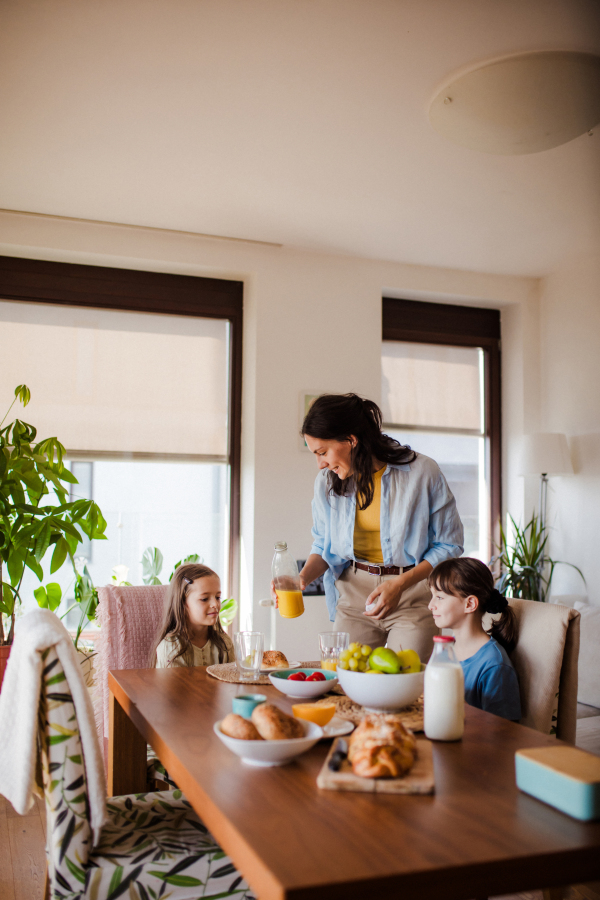 Mother prepares breakfast and pouring juice for the children, in the morning. Maternal love and care for the household and family.