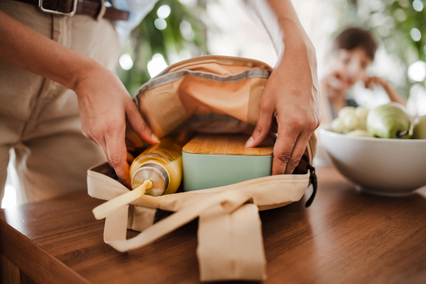 Mother packing school bag for kid. Putting bottle of juice, snacks for her children into school bag. Snack, school lunch in a snack box for school.