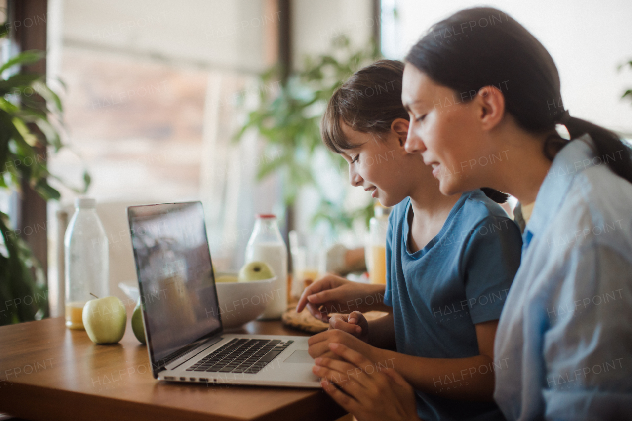 Mom and daughter watching entertaining videos on mom's work laptop. Remote work and home office for single mother with children.