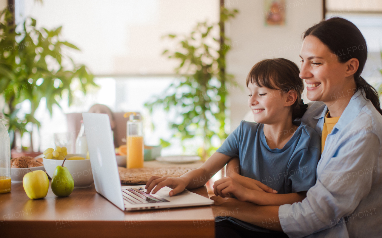 Mom and daughter watching entertaining videos on mom's work laptop. Remote work and home office for single mother with children.