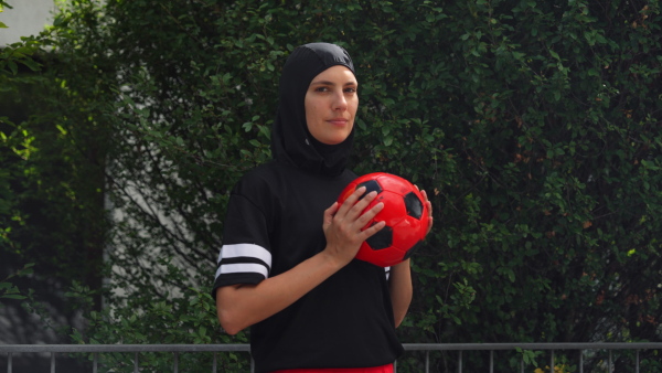 Beautiful female football player in hijab with a ball in her hand. The woman plays soccer for relaxation. Concept of muslim woman in sport.