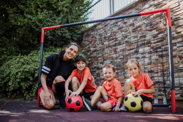 Mom playing football with her children, dressed in football jerseys. The family as one soccer team. Fun family sports activities outside in the backyard or on the street.