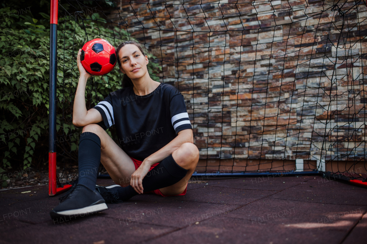 Beautiful female football player standing by the football goal with a ball in her hand. The woman plays soccer for relaxation. Concept of mental health and sport.