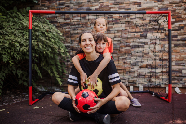 Mom playing football with her daughters, dressed in football jerseys. The family as one soccer team. Fun family sports activities outside in the backyard or on the street.