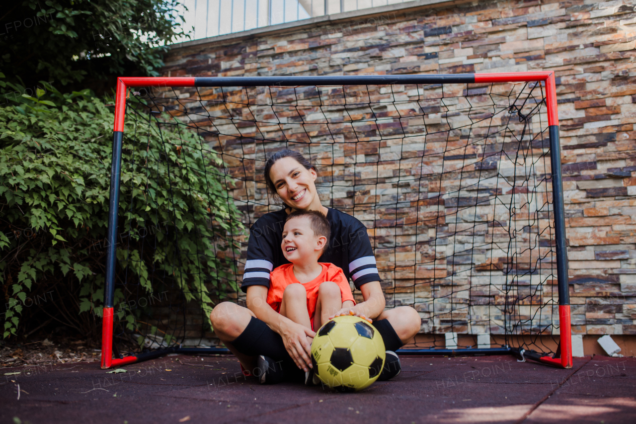 Mom playing football with her son, dressed in football jerseys. The family as one soccer team. Fun family sports activities outside in the backyard or on the street.