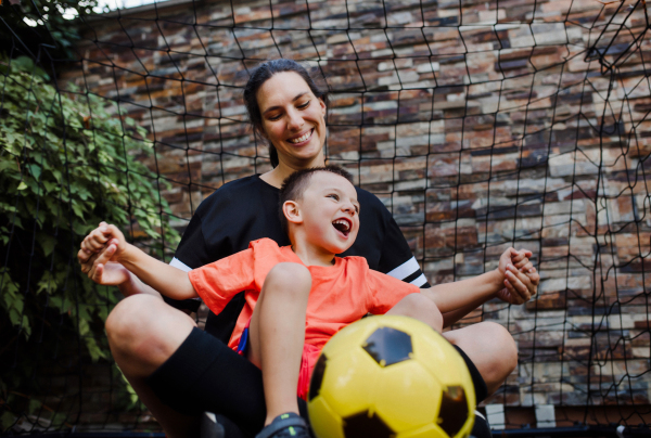 Mom playing football with her son, dressed in football jerseys. The family as one soccer team. Fun family sports activities outside in the backyard or on the street.