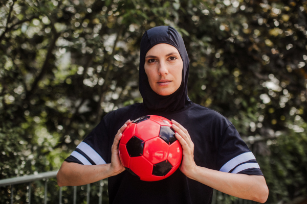 Beautiful female football player in hijab with a ball in her hand. The woman plays soccer for relaxation. Concept of muslim woman in sport.