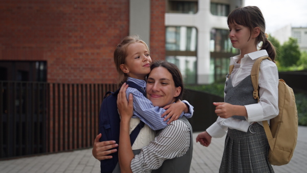 A hard-working, ambitious mother preparing her daughters for school, saying goodbye to them in front of the school building, and heads to work. Concept of work-life balance for women.