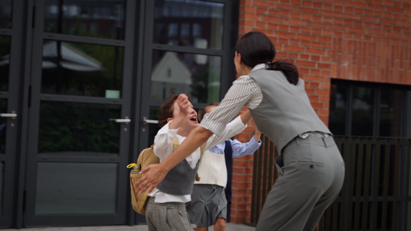 A hard-working, ambitious mother picking up daughters from school, greeting them in front of the school building, and heads to work. Concept of work-life balance for women.