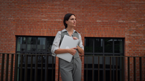 Portrait of beautiful woman in business attire standing on city street. Muslim businesswoman with laptop making call. Female university professor in front of university building.