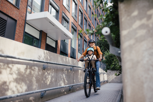 Mother carring her son on a secure child bike carrier or seat, both wearing helmets. Mom commuting with a young child through the city on a bicycle.