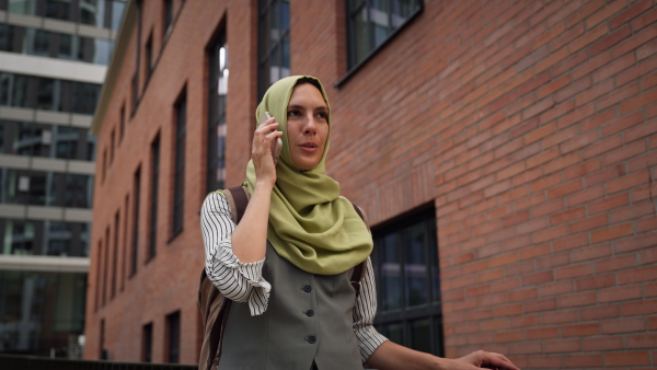 Beautiful woman in hijab making a phone call on a city street. Muslim businesswoman has a business call outside in the city, heading to a meeting.