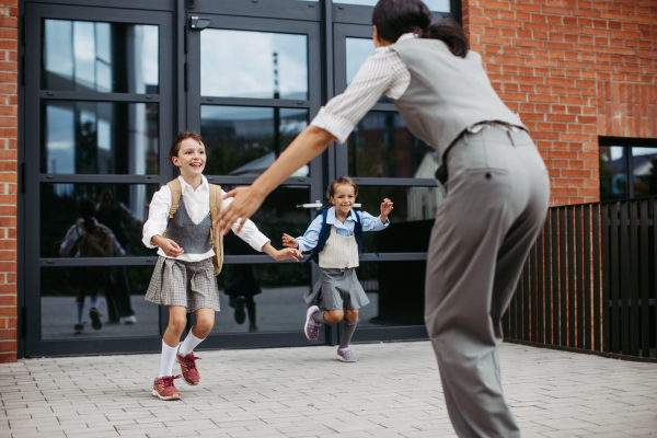 A hard-working, ambitious mother picking up daughters from school, greeting them in front of the school building, and heads to work. Concept of work-life balance for women.