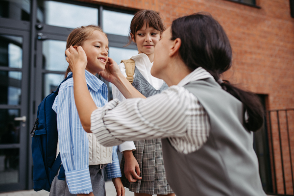 A hard-working, ambitious mother preparing her daughters for school, saying goodbye to them in front of the school building, and heads to work. Concept of work-life balance for women.