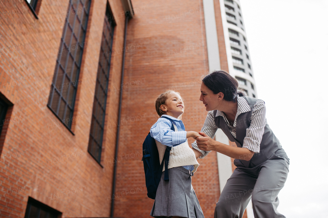 A working mother saying goodbyeto to daughter in front of the school building, and heading to work. Concept of work-life balance for women.