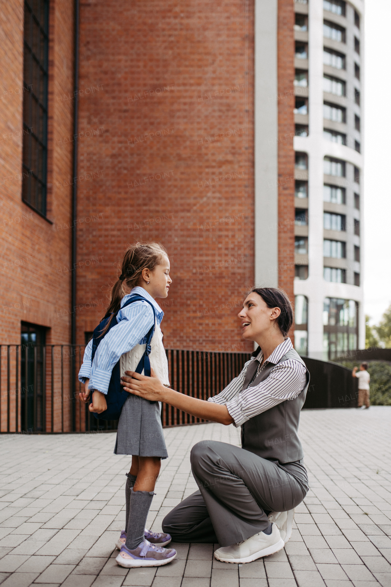 A working mother saying goodbyeto to daughter in front of the school building, and heading to work. Concept of work-life balance for women.