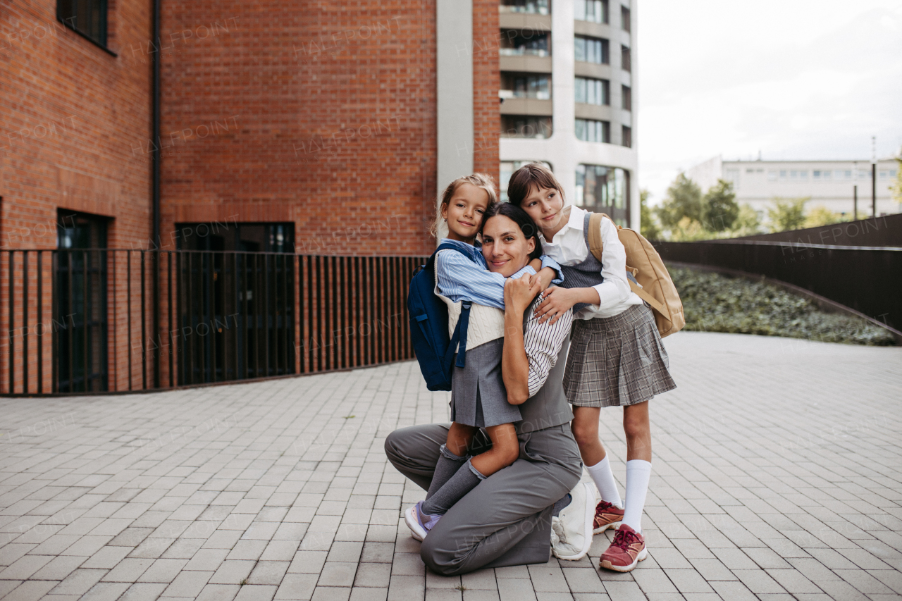 Working mother picking up daughters from school, greeting them in front of the school building, and heads to work. Concept of work-life balance for women.