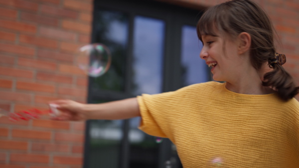 Video of a little girl playing with bubble blower in front of school building.