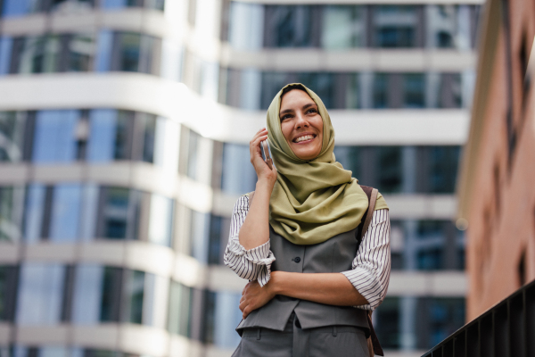 Beautiful woman in hijab making a phone call on a city street. Muslim businesswoman has a business call outside in the city, heading to a meeting.