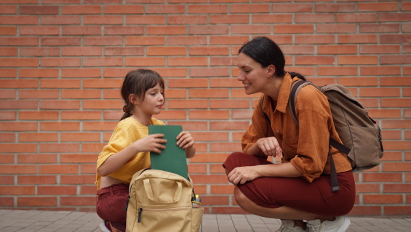 A hard-working, ambitious mother preparing her daughter for school, saying goodbye to her in front of the school building, and heads to work. Concept of work-life balance for women.